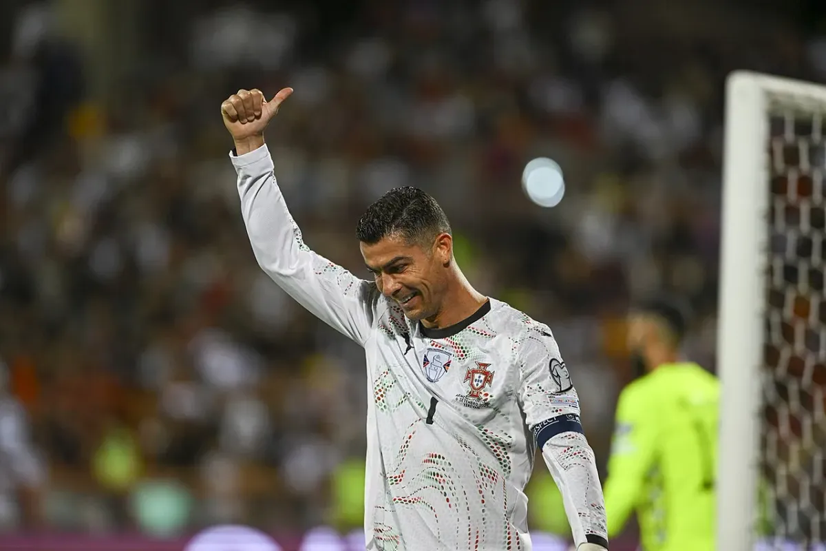 Portekiz'in beyaz forması ve kaptan pazubendiyle Cristiano Ronaldo, sahada bir elini kaldırmış gülümsüyor