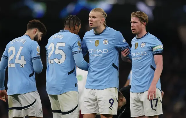 Açık mavi formalı Manchester City oyuncuları maç sırasında sahada yan yana duruyor