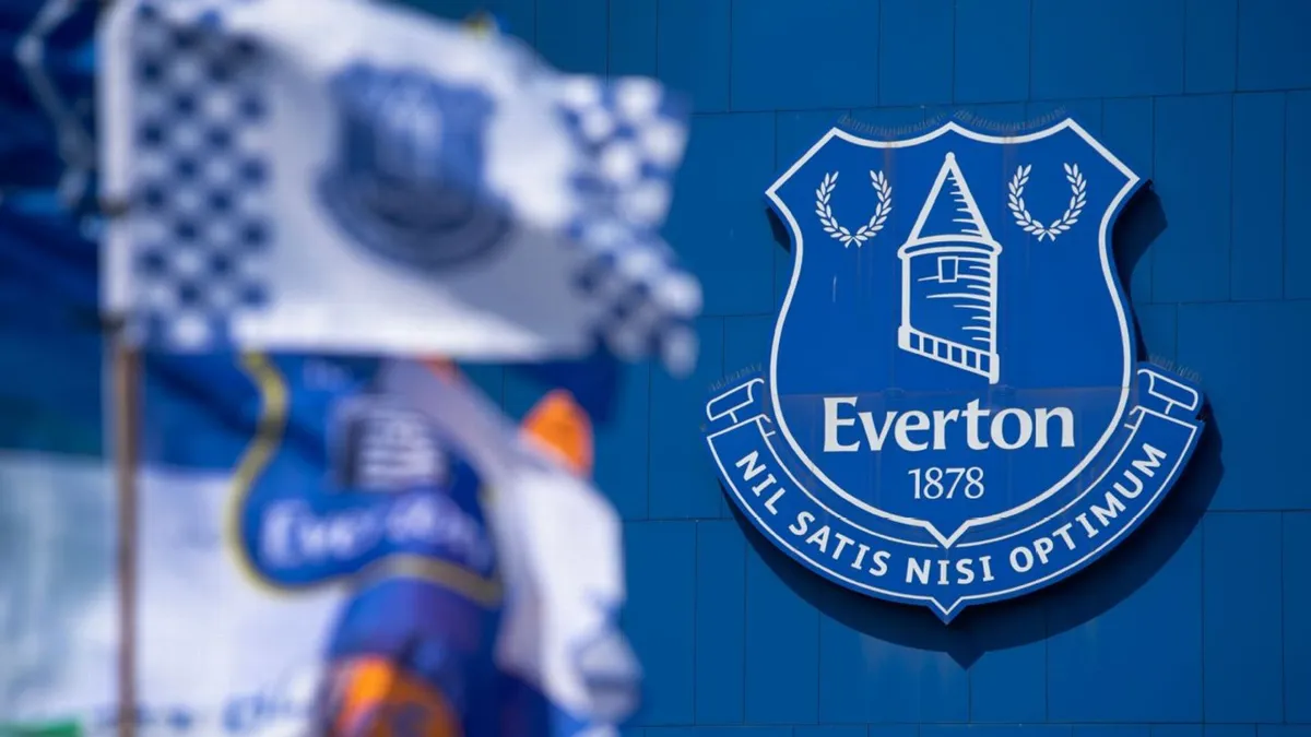 Everton'ın mavi armalı logosu, önünde bulanık Everton bayrakları