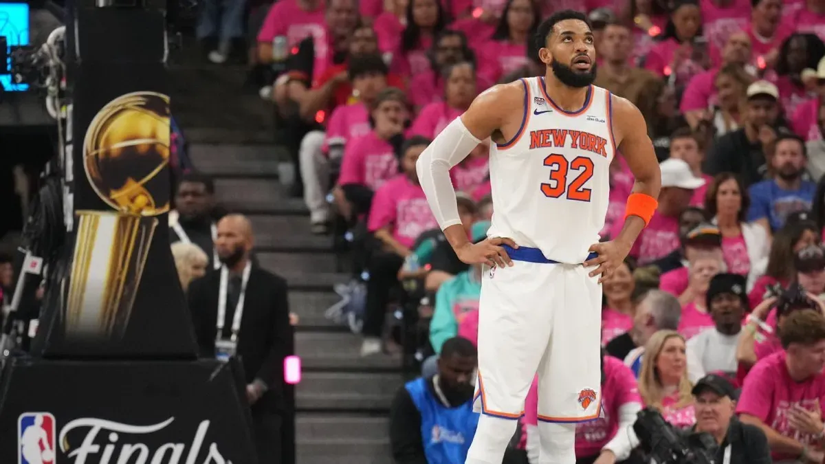 New York Knicks formalı Karl-Anthony Towns, NBA Finalleri kupasının yanında bellerinde elleriyle bekliyor