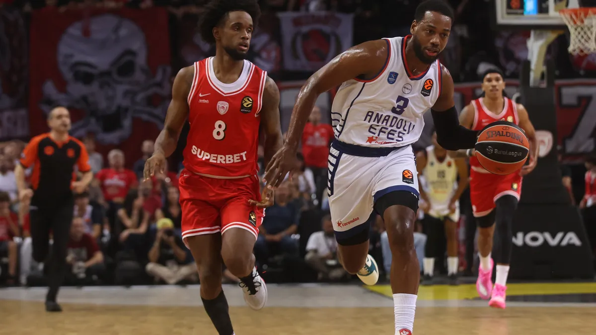Anadolu Efes'in 3 numaralı oyuncusu, kırmızı formalı Olympiakos oyuncusunun önünde topu hücuma taşıyor