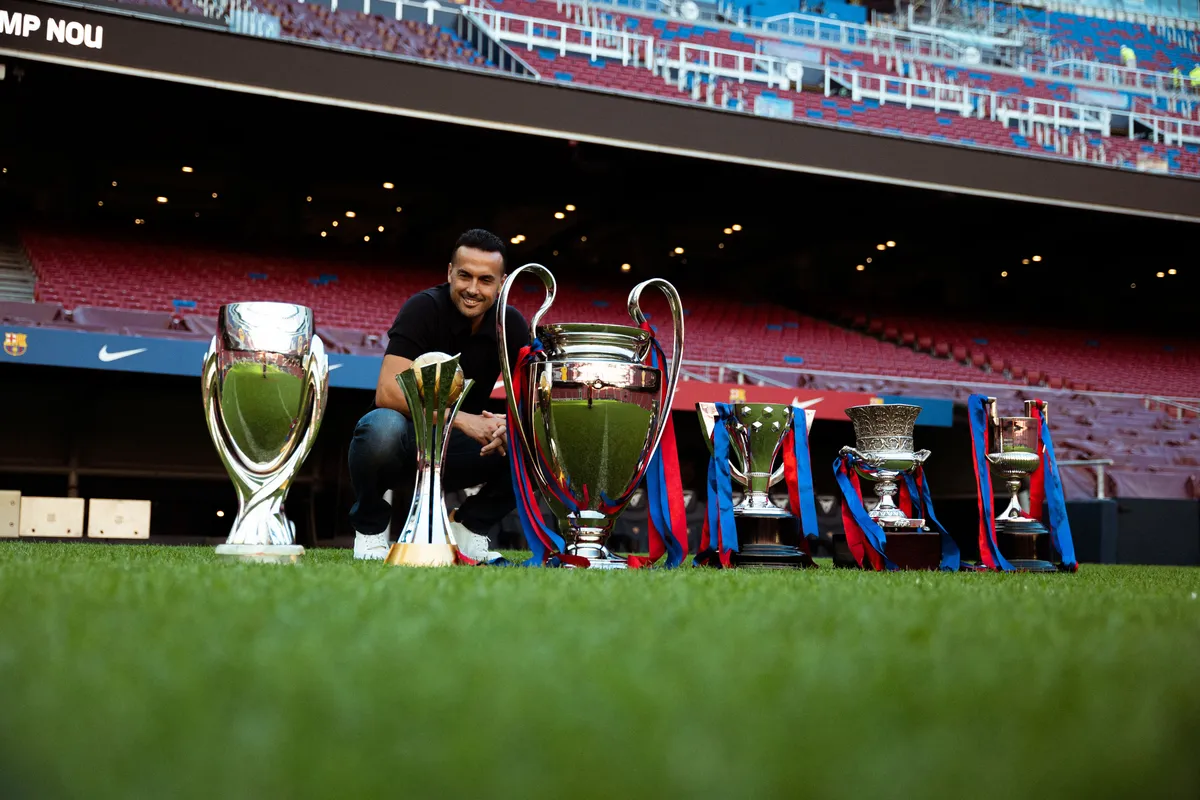 Pedro, Camp Nou'nun çim sahasında Barcelona'yla kazandığı kupaların yanında çömelmiş poz veriyor
